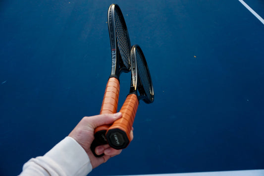 Holding two black tennis rackets on a blue court with leather handles