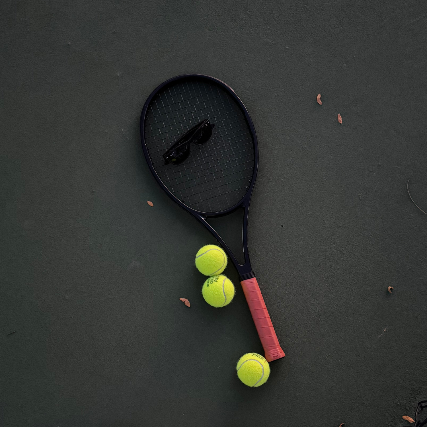 Black tennis racket with sunglasses on green court