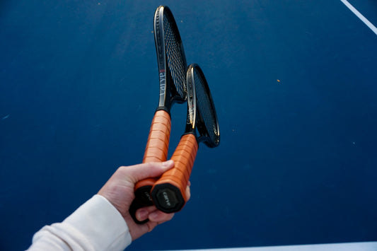 Holding two black tennis rackets on a blue court with leather handles