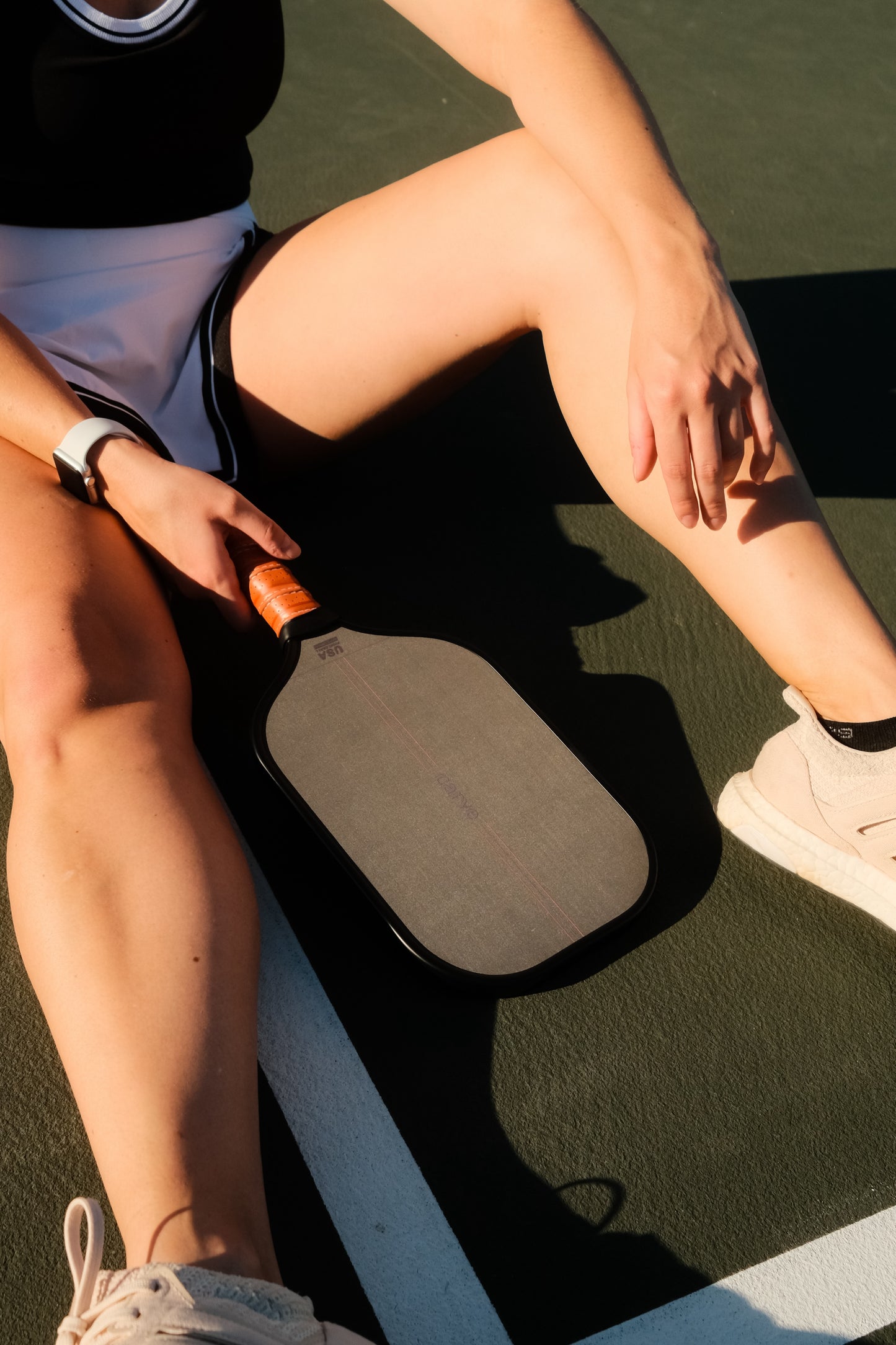 Woman with Carve AllCourt 14mm paddle between legs on pickleball court