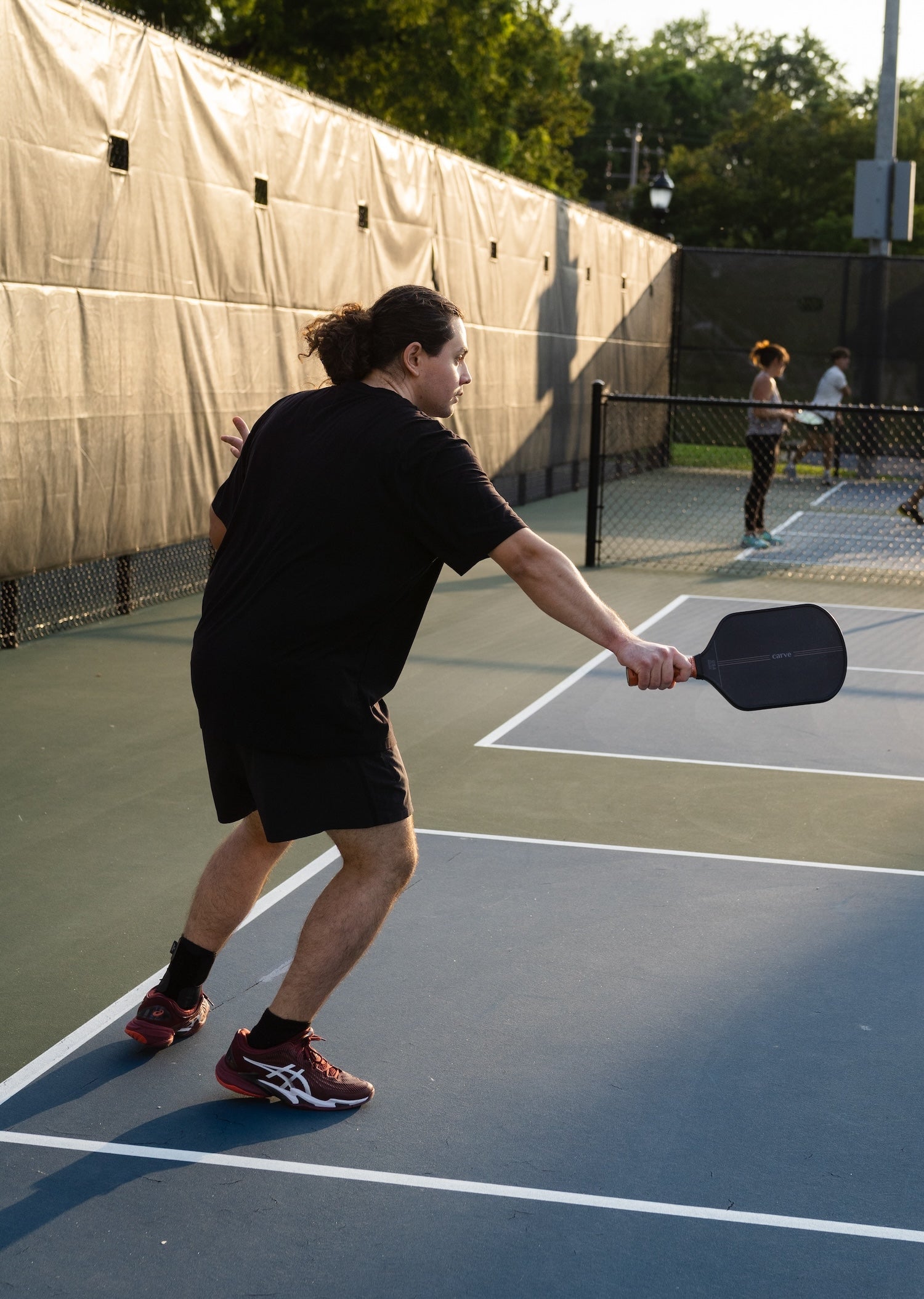 White male with long hair on a pickleball court with a Carve AdTouch 16mm Paddle